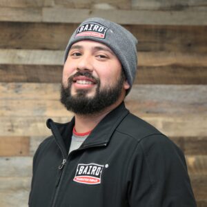 Headshot of installer, Albert Garza, taken at the San Antonio office. He is smiling and wearing a black Baird jacket and grey Baird beanie.