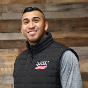 Headshot of sr. system design specialist. Brandon Villanueva, taken at the San Antonio office. He is smiling and wearing a black Baird puffer vest.