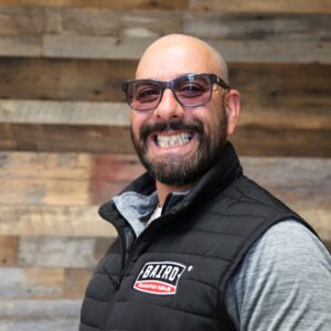 Headshot of assistant production manager, Diego DiMatteo, taken at the San Antonio office. He is smiling and wearing a black Baird puffer vest.