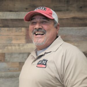 Headshot of foreman, Jesus Garza, taken at the San Antonio office. He is smiling and wearing a pale yellow Baird polo and a red and white Baird baseball cap.
