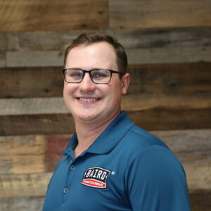 Headshot of San Antonio Baird Foundation Repair Sr. System Design Specialist, Kelby Beard, taken at the San Antonio office. He is smiling and wearing a dark blue Baird polo shirt.