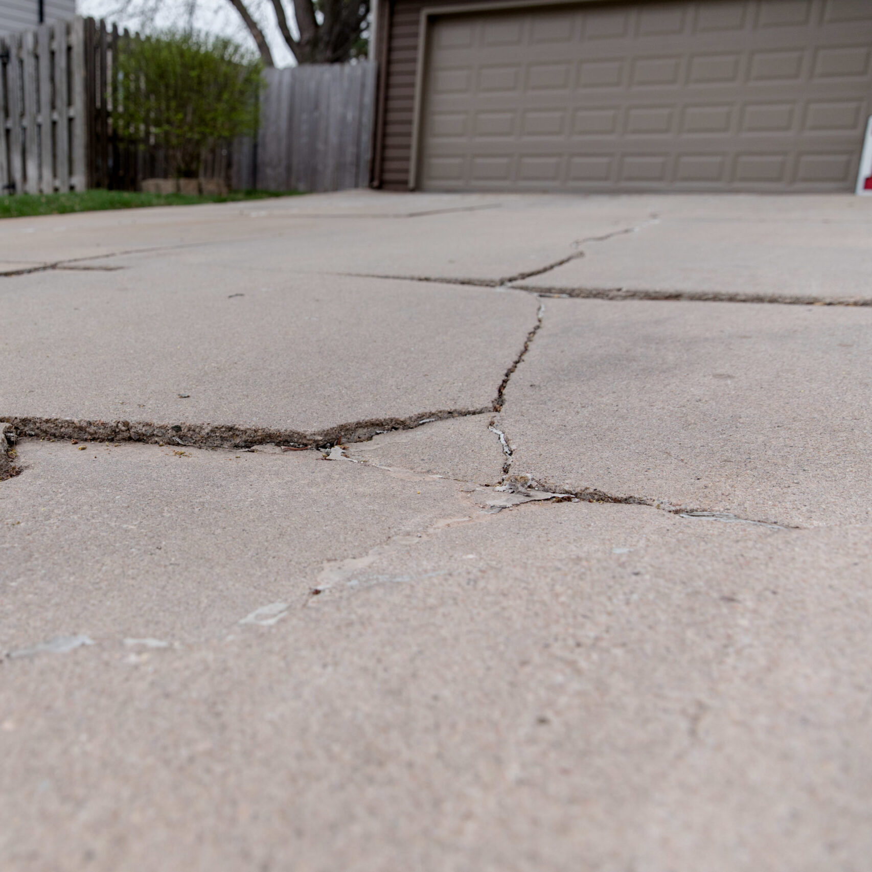 Close up of concrete cracks in a driveway with a brown garage door.