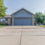 View of an uneven concrete driveway in front of a brick home with a blue garage door.
