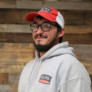 Headshot of co-foreman, Michael Tavera, taken at the San Antonio office. He is smiling and wearing a light grey Baird hoodie and red and white Baird baseball cap.