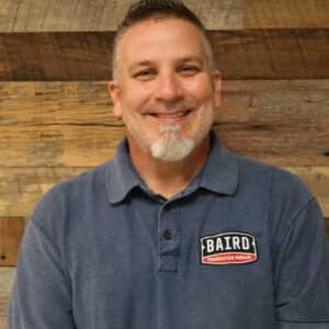 Headshot of Service specialist, Rusty Fisher, taken at the San Antonio office. He is smiling and wearing a gray Baird collared shirt.