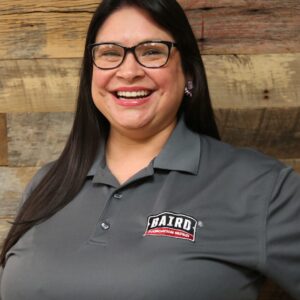 Headshot of production assistant, Shakira Deleon, taken at the San Antonio office. She is smiling and wearing a gray Baird polo shirt.