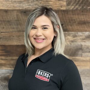 Headshot of customer care specialist, Roxanne Rodriguez, taken at the San Antonio office. She is smiling and wearing a black Baird polo shirt.