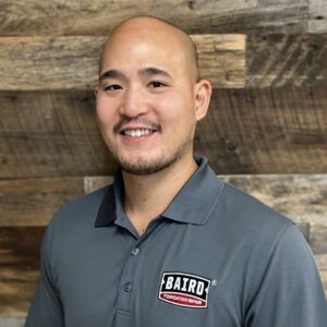 Headshot of system design specialist, Tim Yan, taken at the San Antonio office. He is smiling and wearing a dark gray Baird Foundation Repair polo shirt.