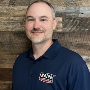 Headshot of system design specialist, Nate Howell, taken at the San Antonio office. He is smiling and wearing a navy Baird Foundation Repair polo shirt.