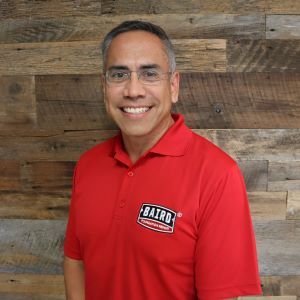 Small headshot of system design specialist, Rey Rodriguez, taken at the Corpus Christi office. He is smiling, wearing rimless glasses, and wearing a red Baird Foundation Repair polo shirt.