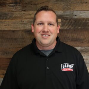Headshot of system design specialist, Justin Hollis, taken at the Houston office. He is smiling and wearing a black Baird Foundation Repair polo shirt.