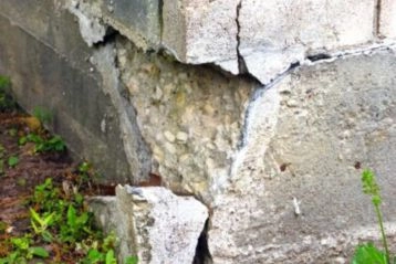 Close up of a large chunk of concrete broken off the corner of a foundation slab below where brick siding begins.