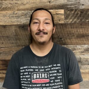 Headshot of installer, Jesus Garcia, taken in the San Antonio office. He is wearing a black Baird Foundation Repair t-shirt with the team message printed on it.