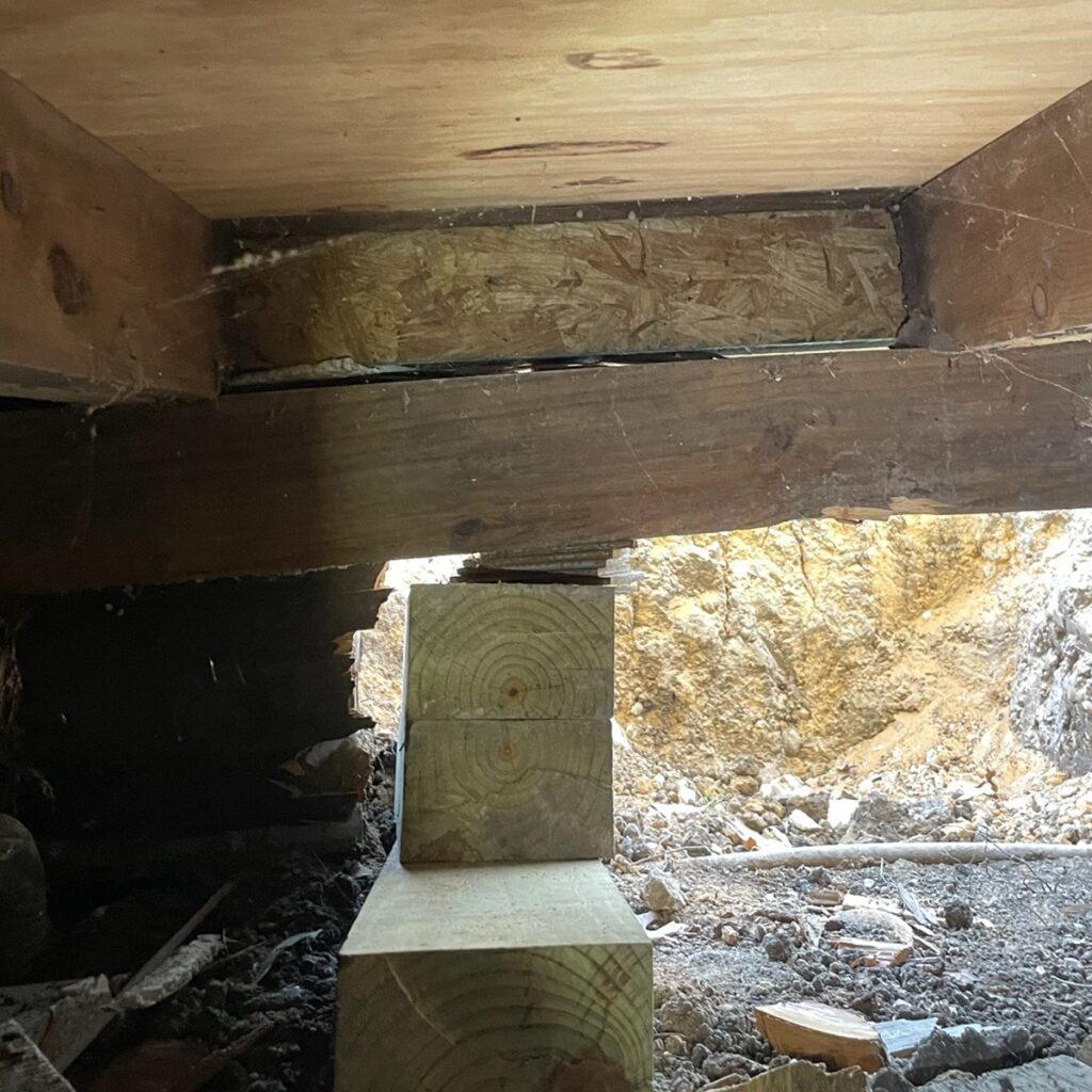 View of thin, flat, wooden shims installed underneath a home's wooden pier and beam foundation, causing the home to be unleveled.