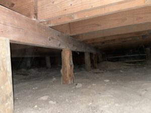 View of a crawlspace underneath with old wooden pier and beam foundation.