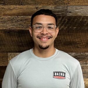 Headshot of co foreman, Mark Pardo, taken in the San Antonio office. He is smiling and wearing a gray Baird Foundation Repair t-shirt and clear-rimmed glasses.