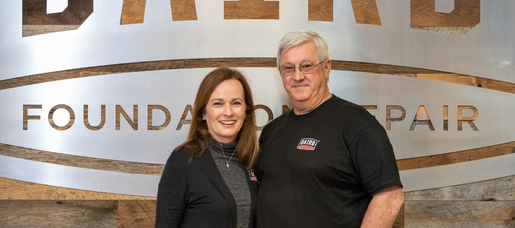 john and melanie chaney standing in front of the silver baird logo in their office