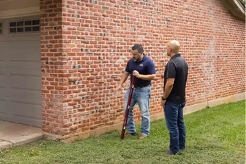 A contractor and a customer inspecting exterior brick wall damage on residential home