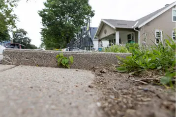 Uneven sidewalk in Terrell Hills with raised concrete creating a tripping hazard near a residential home