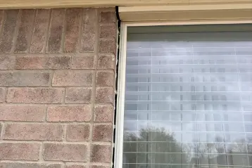 Vertical crack between brick exterior wall and window frame on a residential home, showing foundation or settling damage