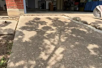 Uneven concrete driveway apron near a garage entrance in Pflugerville, Texas, showing a raised slab that created a trip hazard for visitors.