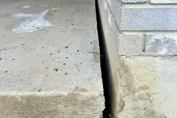 Close-up of a concrete porch slab separating from a cinder block foundation wall, showing a deep gap before repair