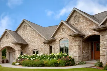 Home featuring white hydrangea shrubs and mixed perennial plantings along the curved front foundation bed under a partly cloudy blue sky.